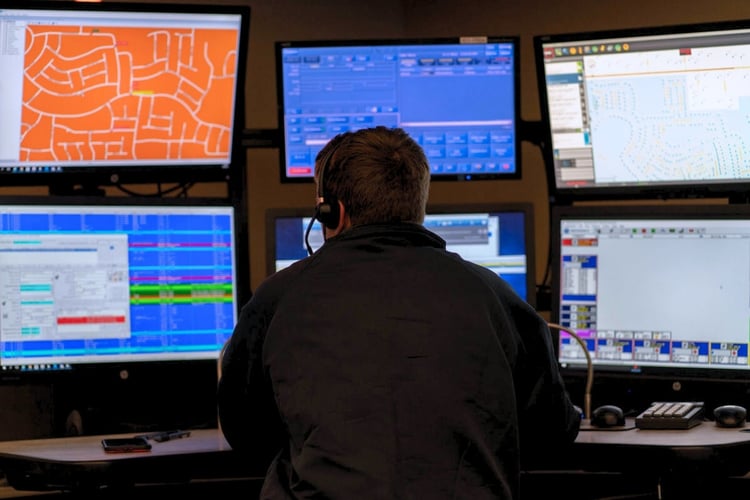Operator monitoring multiple real-time data feeds and analytics dashboards in a centralized command center environment