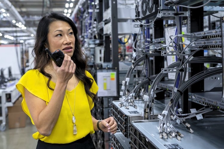 Communications technician using a two-way radio beside DAS and radio network equipment in a commercial building