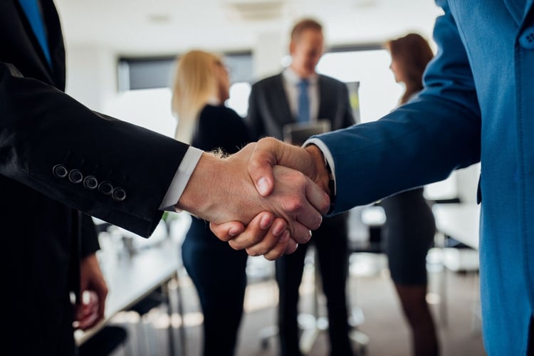 Business professionals shake hands during a meeting, representing the partnership between Chicago Communications and CSE Crosscom.
