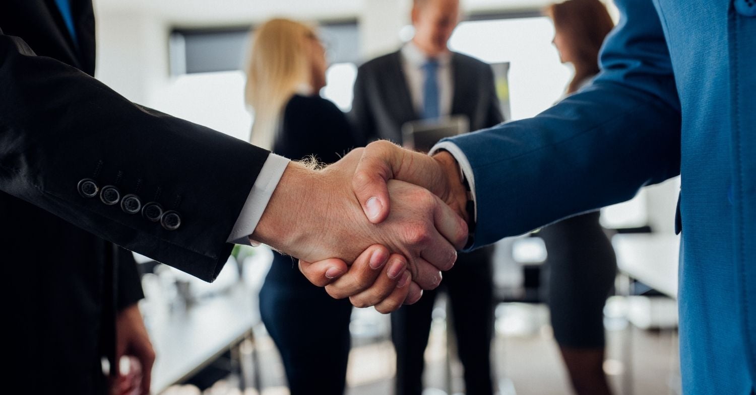 Business professionals shake hands during a meeting, representing the partnership between Chicago Communications and CSE Crosscom.